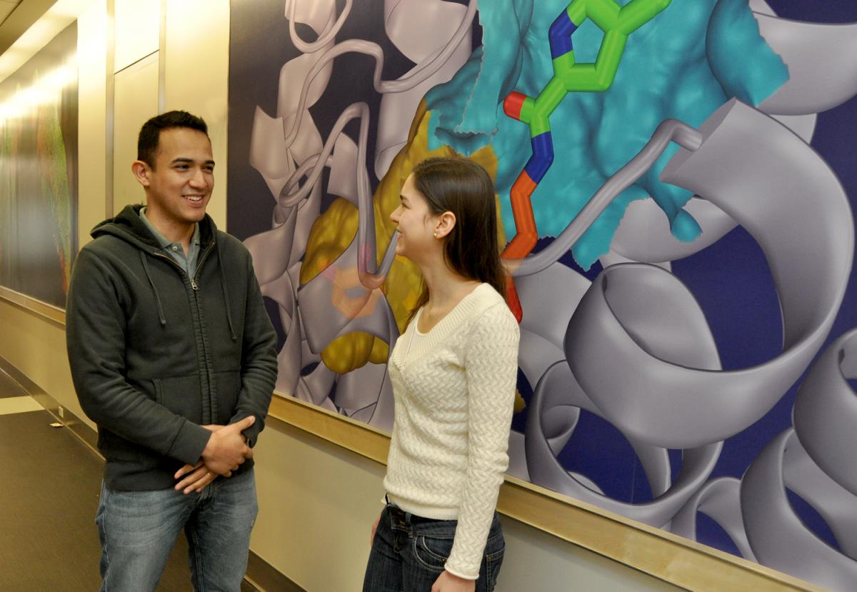 A guy talking to a girl about something in front of a painting.